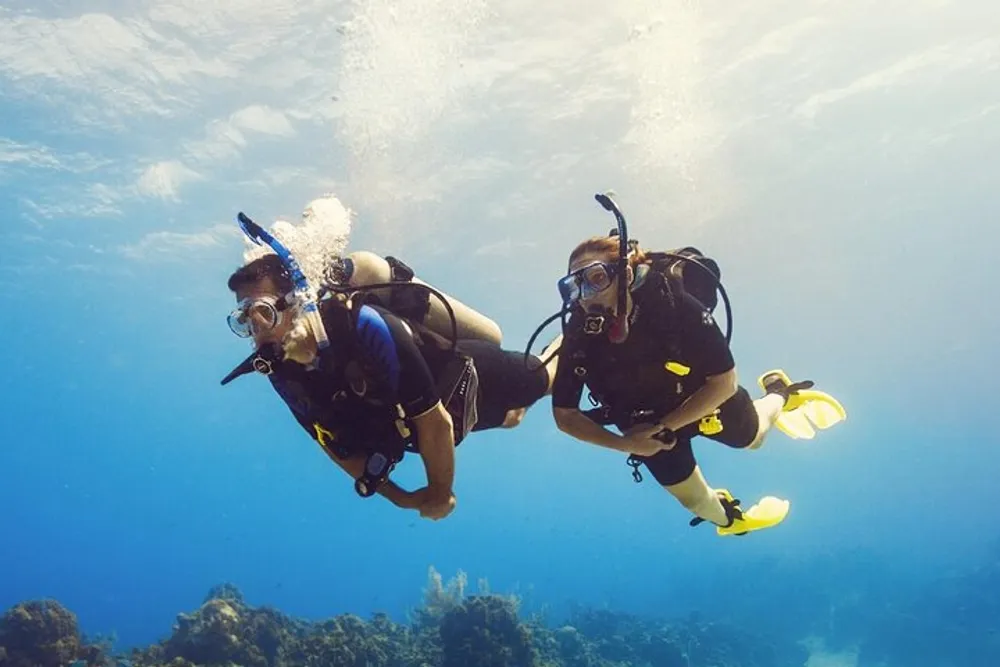 Two scuba divers are exploring underwater surrounded by clear blue water and bubbles from their breathing apparatus