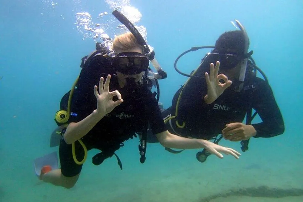 Two scuba divers are underwater giving the OK hand signal