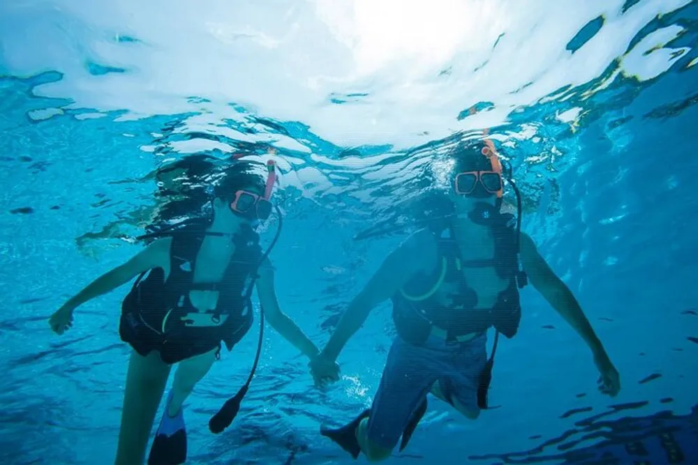 Two scuba divers are swimming underwater side by side in clear blue water