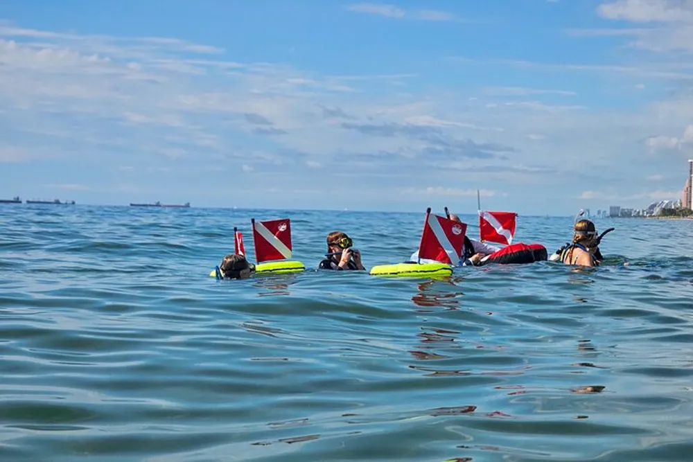 A group of divers with red and white dive flags are floating on the surface of the sea preparing for or returning from an underwater excursion