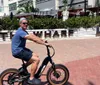 A man is riding a BMX bike on a sunny urban pathway with a sign reading THE WHARF in the background
