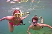Two people are enjoying snorkeling underwater, equipped with fins and diving masks, as they pose for a fun photo.