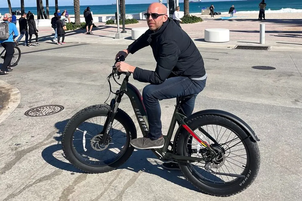 A person is riding a fat-tire electric bike along a sunny coastal promenade