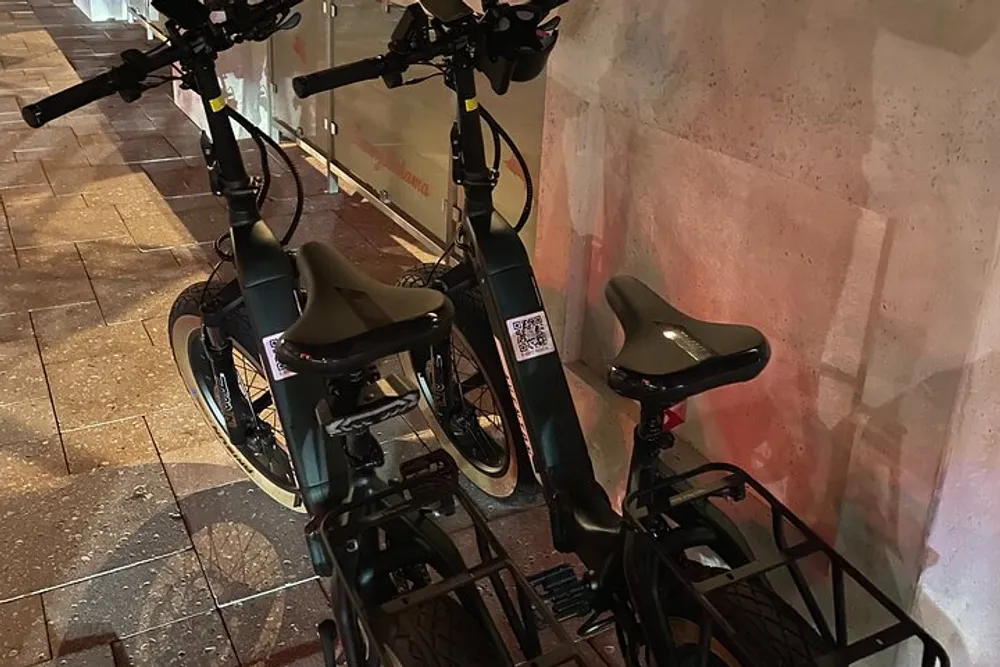 The image shows a row of parked electronic bicycles on a city sidewalk at night illuminated by street lighting