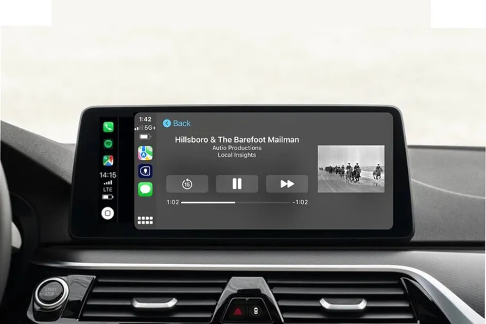 The image shows a cars infotainment screen displaying an interface resembling Apple CarPlay with audio playback controls for a track titled Hillsboro  The Barefoot Mailman