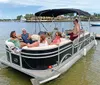 A group of people relax and enjoy a sunny day aboard a pontoon boat on calm waters with waterfront properties in the background