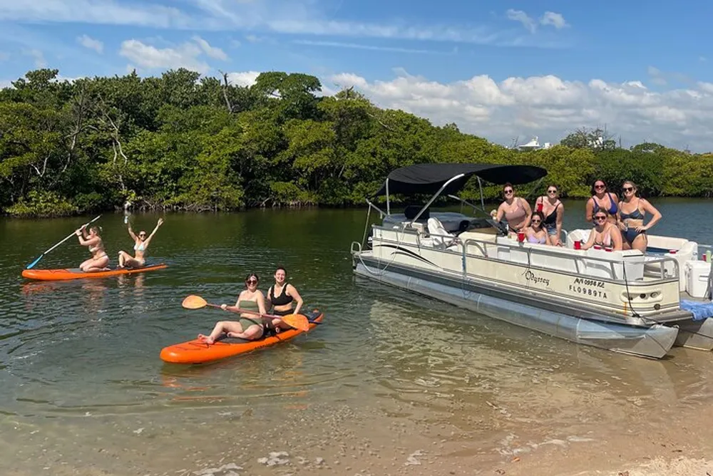 A group of people are enjoying a sunny day outdoors with some lounging on a pontoon boat and others paddling kayaks near a mangrove shoreline