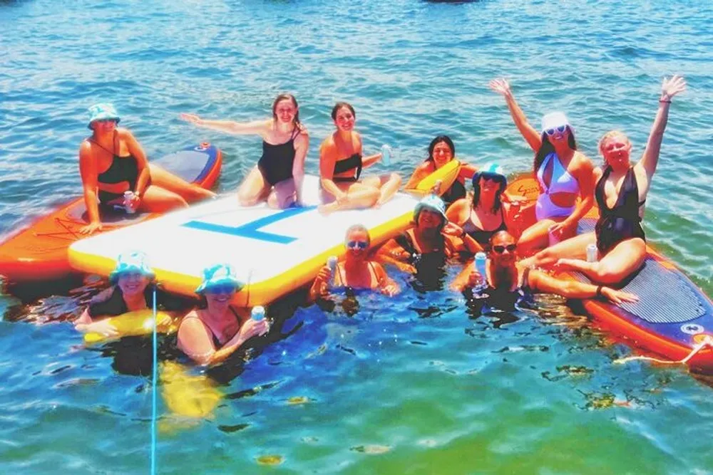 A group of people is happily gathered around and on top of large paddleboards in the water suggesting a social or recreational activity