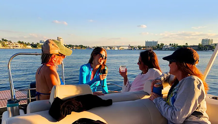 A group of friends is enjoying a boat ride and drinks on a sunny day with a scenic waterfront backdrop.