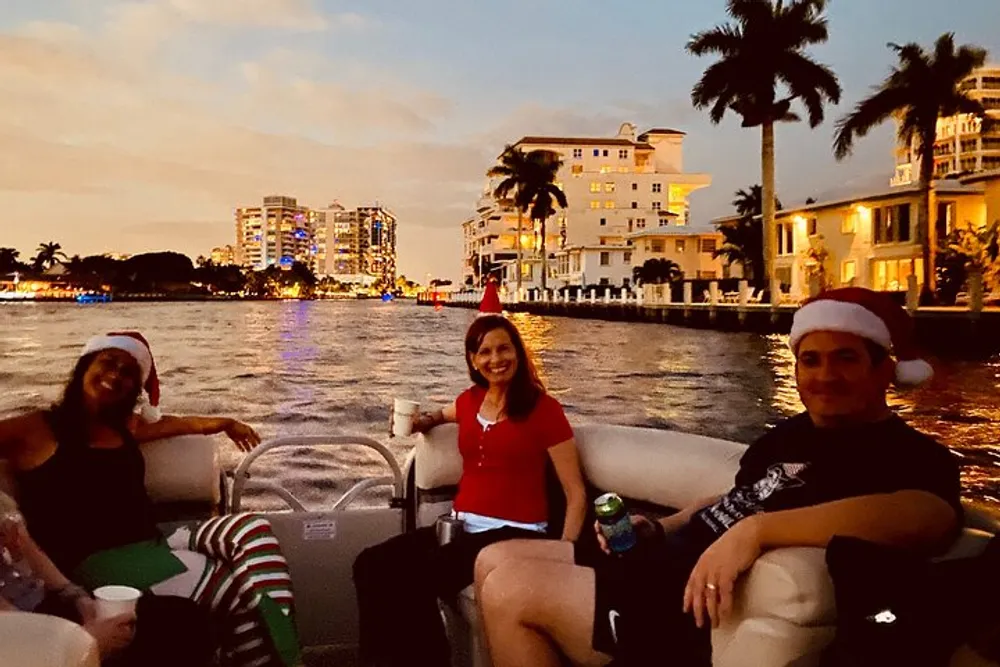 Three people are enjoying a boat ride on a river with festive hats as the evening skyline lights up in the background