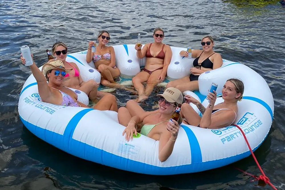 A group of people are relaxing on a large inflatable raft in the water each with a drink in hand