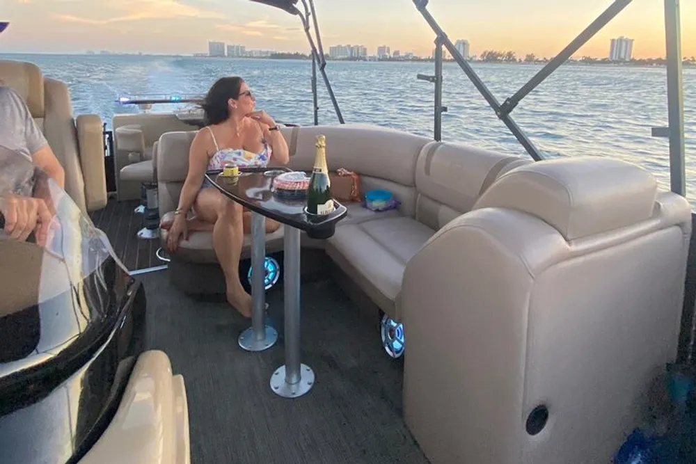A person is enjoying a snack and a glass of drink aboard a boat with plush seating during a scenic evening cruise