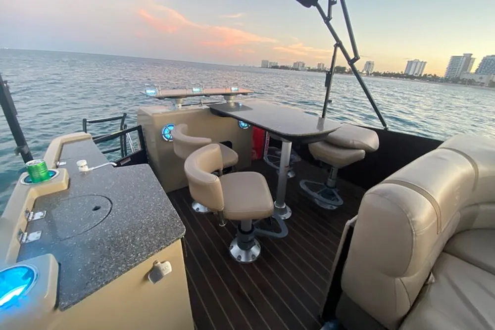 The image shows a luxurious boat interior with comfortable seating and a bar area set against the backdrop of the ocean at dusk