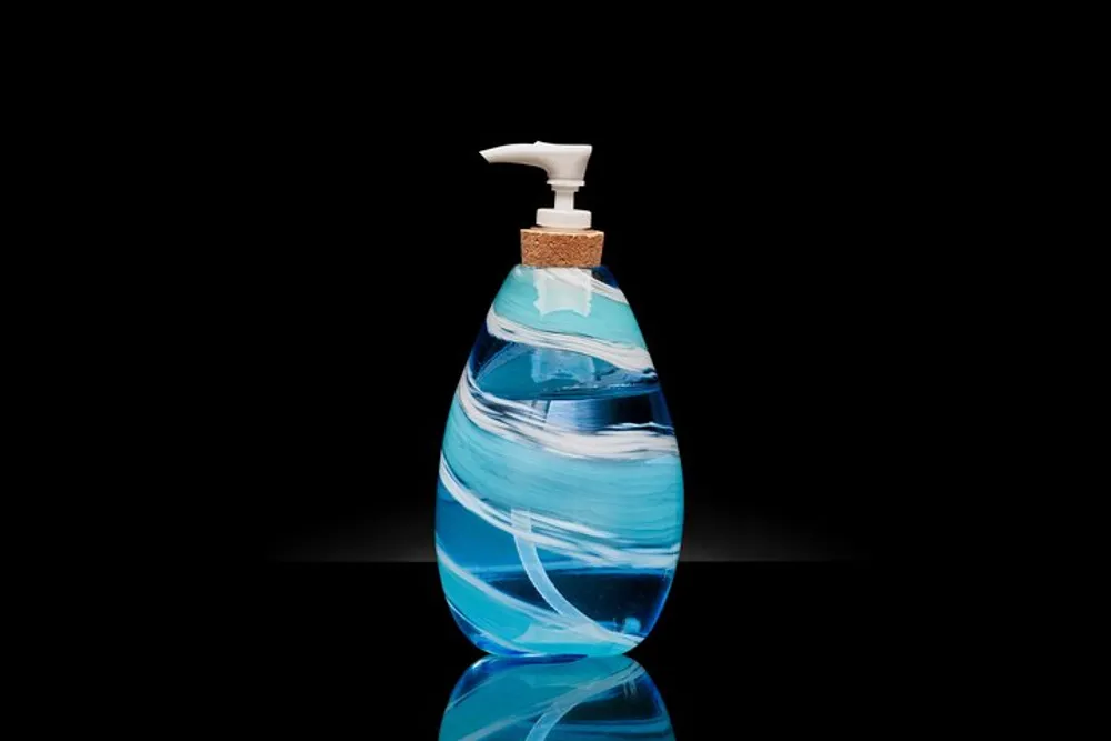 The image features an elegantly designed blue and white swirled liquid soap dispenser with a white pump and cork detail set against a reflective black surface and background