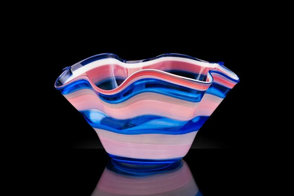 An elegant glass vase with wavy edges features a swirl of pink blue and clear stripes presented against a black background with a reflective surface
