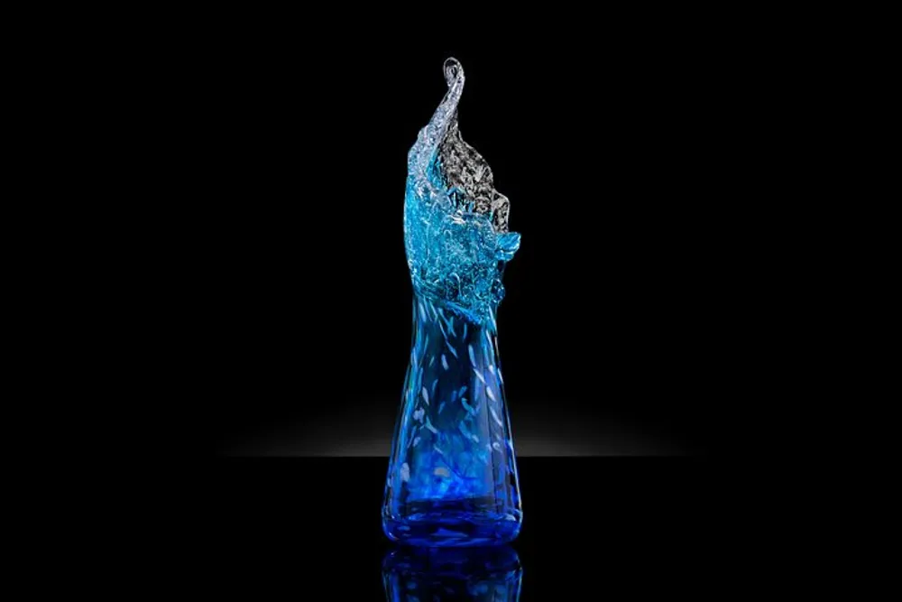 The image shows a blue glass bottle with a dynamic splash of water captured mid-air against a dark background