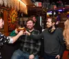 A group of people are toasting with drinks and smiling at a lively bar decorated with colorful wall art