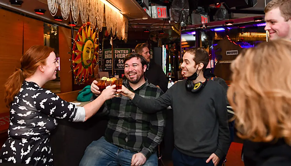 A group of people are toasting with drinks and smiling at a lively bar decorated with colorful wall art