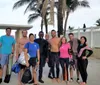 A group of smiling people in swimwear and diving gear are posing together in front of palm trees likely about to go or having returned from a dive