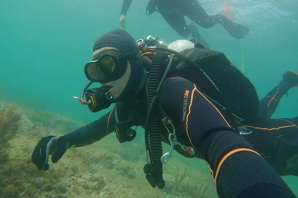 A scuba diver is submerged in clear water exploring an underwater environment equipped with a full dive suit mask fins and breathing apparatus