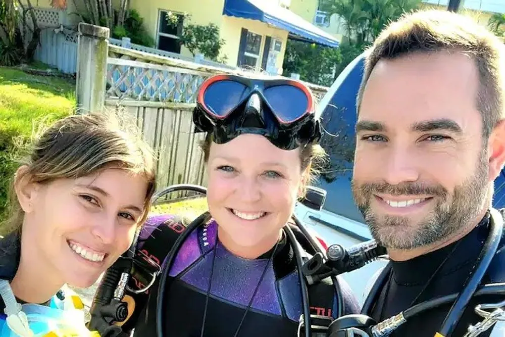 Three people in diving gear are posing for a selfie with bright smiles suggesting they are about to embark on a scuba diving adventure