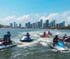 A group of people are riding jet skis on a body of water with a city skyline in the background