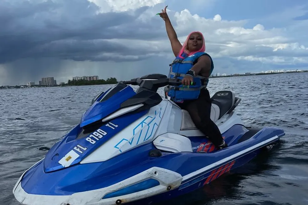 A person is posing with one arm raised while sitting on a jet ski on the water with dark clouds looming in the background