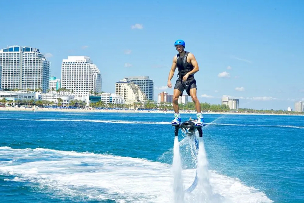 A person is hoverboarding above the water near a coastal cityscape under a clear blue sky