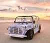 A light blue beach buggy is parked on the sand with a beautiful ocean sunset in the background