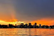 The image shows a vibrant sunset with orange and blue skies over a city skyline reflected on a large body of water.