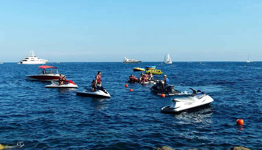 The image captures a bustling water scene with people engaged in various recreational activities on jet skis and boats against a backdrop of larger vessels and a clear blue sky.