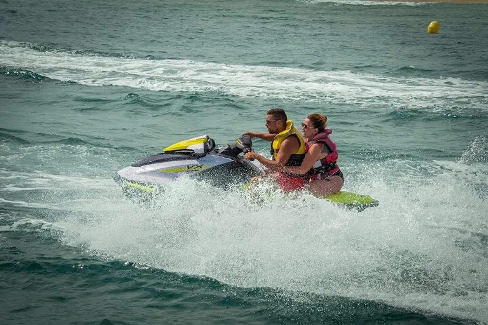 Two people are riding a yellow and purple jet ski over choppy waters creating a spray of water behind them