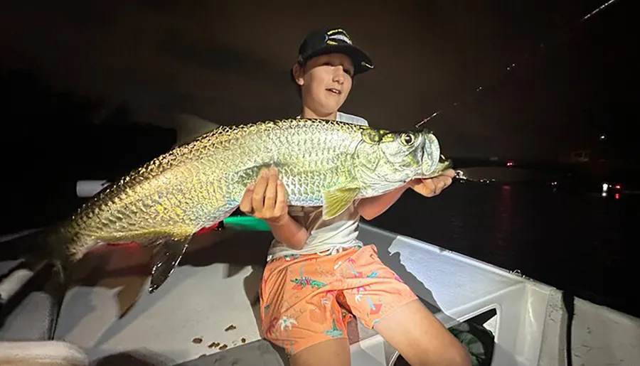 A person is proudly holding a large fish on a boat during nighttime.