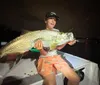 A person is proudly displaying a large fish they caught at night on a boat