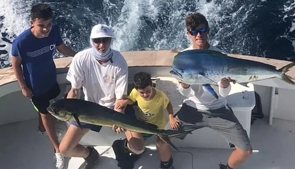 Four individuals on a boat are holding two large fish proudly displaying their catch