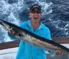 A person is holding a large fish with a big smile on their face standing on a boat with the ocean in the background