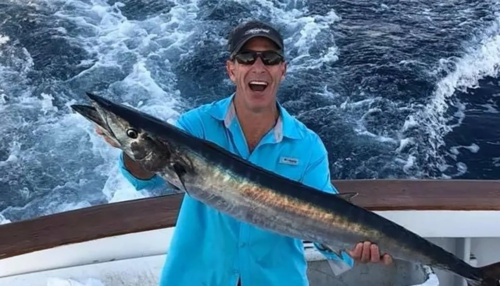 A person is holding a large fish with a big smile on their face standing on a boat with the ocean in the background