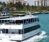 A sightseeing tour boat named ISLAND QUEEN is cruising along a waterway with passengers on board with tropical buildings and palm trees in the background