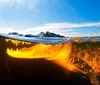 The image shows a split-level view of a crocodile submerged underwater with its jagged teeth visible against a backdrop of a clear sky and mountains above the surface