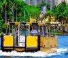 A water taxi with passengers is cruising along a river surrounded by lush tropical foliage