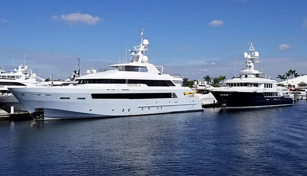 The image shows several large luxury yachts moored in a calm marina under a clear blue sky