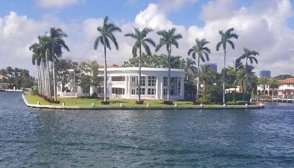 A luxurious white house stands on a lush green palm-fringed peninsula surrounded by water