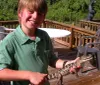 A smiling boy is holding a small alligator on a sunny deck with outdoor furniture in the background