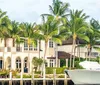 A person is looking towards a waterfront property lined with palm trees from a boat