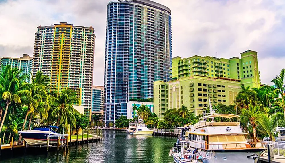 The image shows a vibrant waterfront scene with modern high-rise buildings and luxury boats moored along a palm-lined canal
