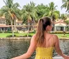 A person is looking towards a waterfront property lined with palm trees from a boat