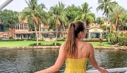 A person is looking towards a waterfront property lined with palm trees from a boat.