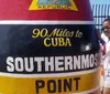 A person is posing next to the iconic Southernmost Point buoy in Key West Florida with the text 90 Miles to Cuba