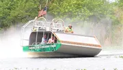 A group of people are enjoying a ride on an airboat gliding through a waterway, likely in a swamp or wetlands area.