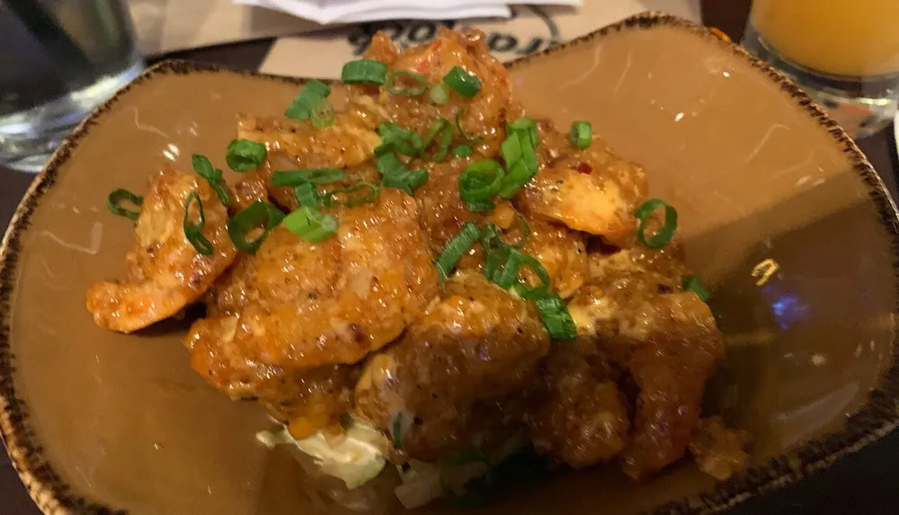 The image shows a plate of crispy chicken bites generously topped with a tangy sauce and sprinkled with sliced green onions served on a bed of lettuce